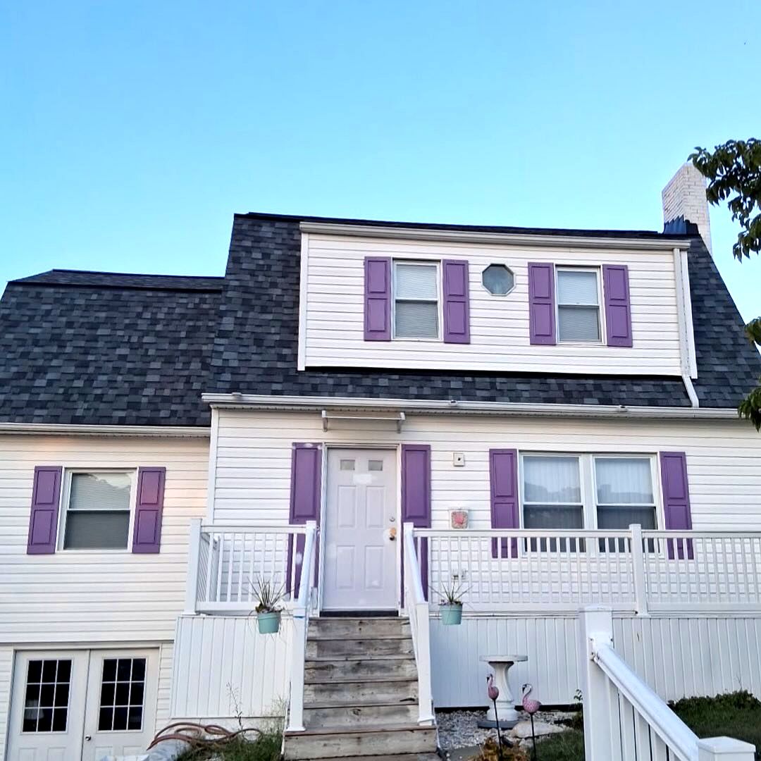 White Cape Cod home with purple shutters and a new charcoal roof