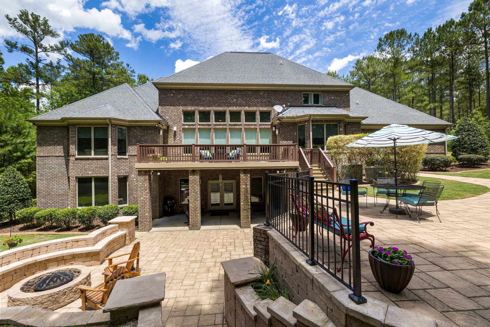 Brick home with a raised deck, black metal railing and a stone patio with a fire pit below