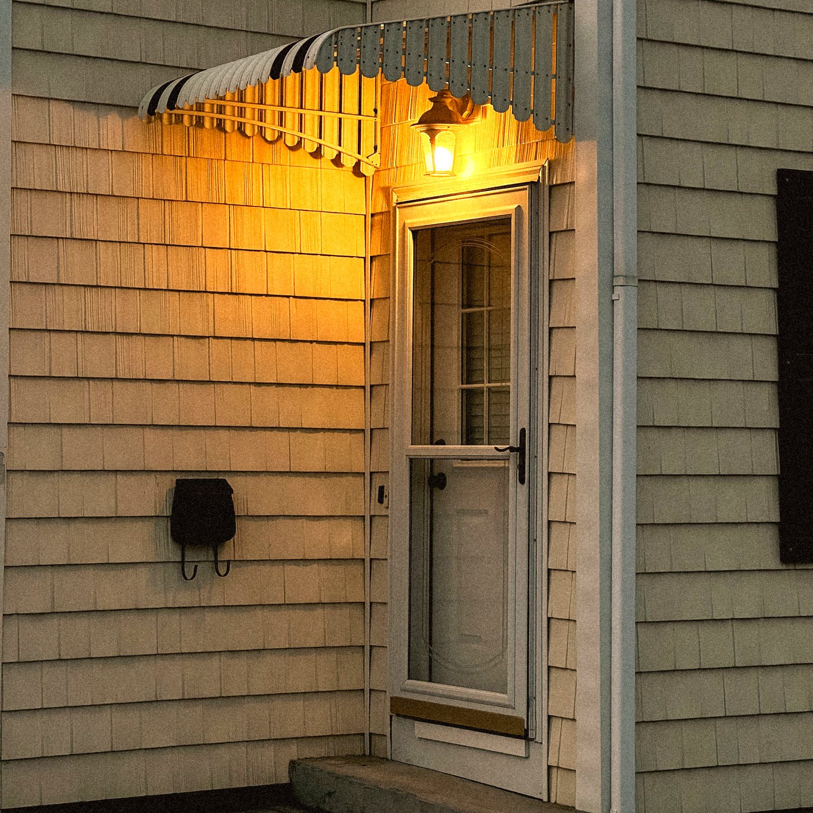 Full-view glass storm door over the entry under a striped awning