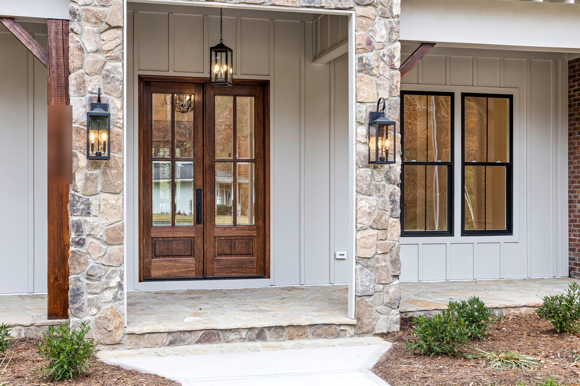 Wood and glass double entry doors with lantern sconces on a stone and board-and-batten front