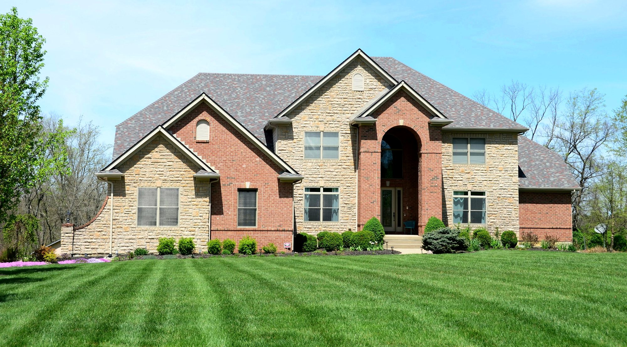 Large brick and stone estate home with an architectural shingle roof and a manicured lawn